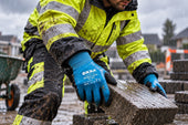 Stratenmaker legt een natte bestratingssteen met OXXA Double-Latex 50-400 werkhandschoenen in de regen