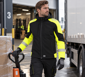 Reflecterende softshell werkjas met capuchon Tricorp 406111 zwart fluorgeel, gedragen op het laadperron van een magazijn